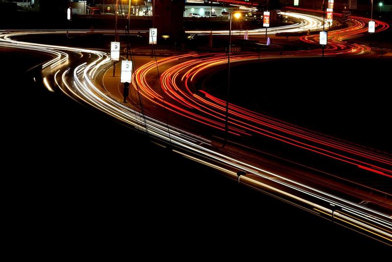 Red and white light trails curving along a highway at night