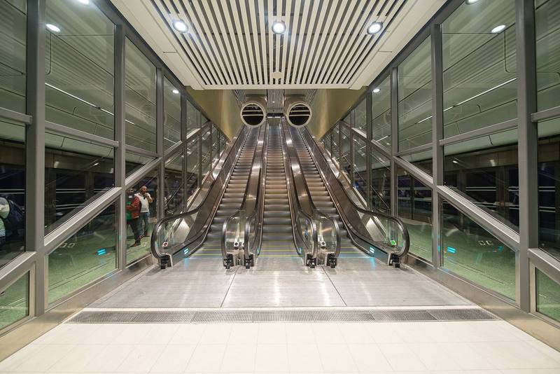 Symmetrical bank of escalators in a bright, glass-walled metro station