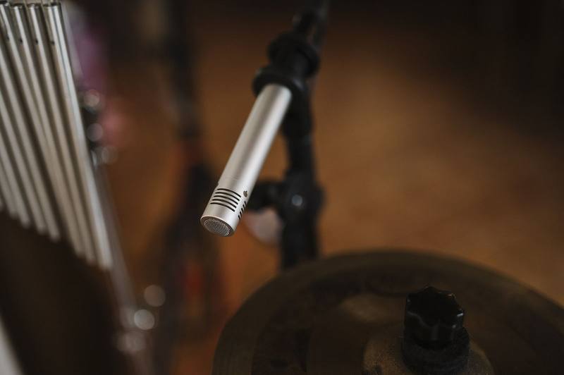 Condenser microphone on a stand above a cymbal in a dim studio