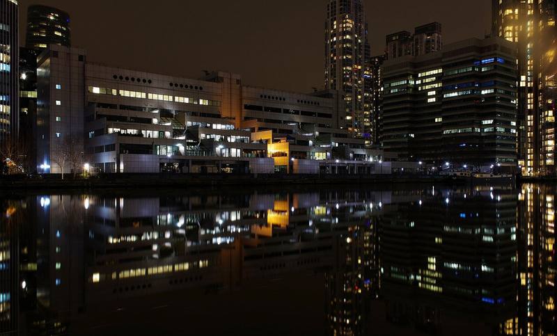 Office towers with lit windows mirrored in still water at night