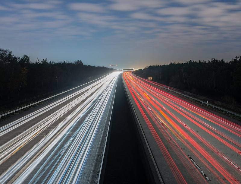 Long-exposure light trails on a motorway through a forest at twilight