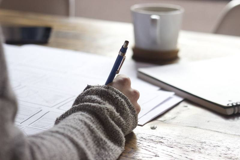 Hand sketching interface wireframes on paper beside a coffee mug